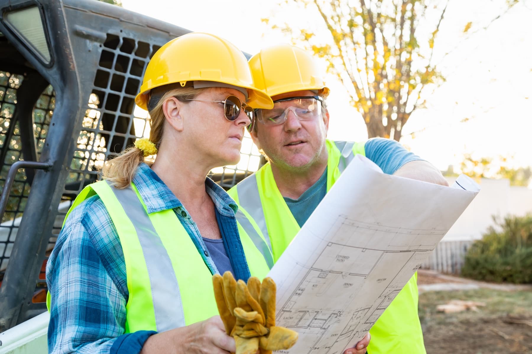 Male and female construction workers reviewing technical blueprints on a jobsite.