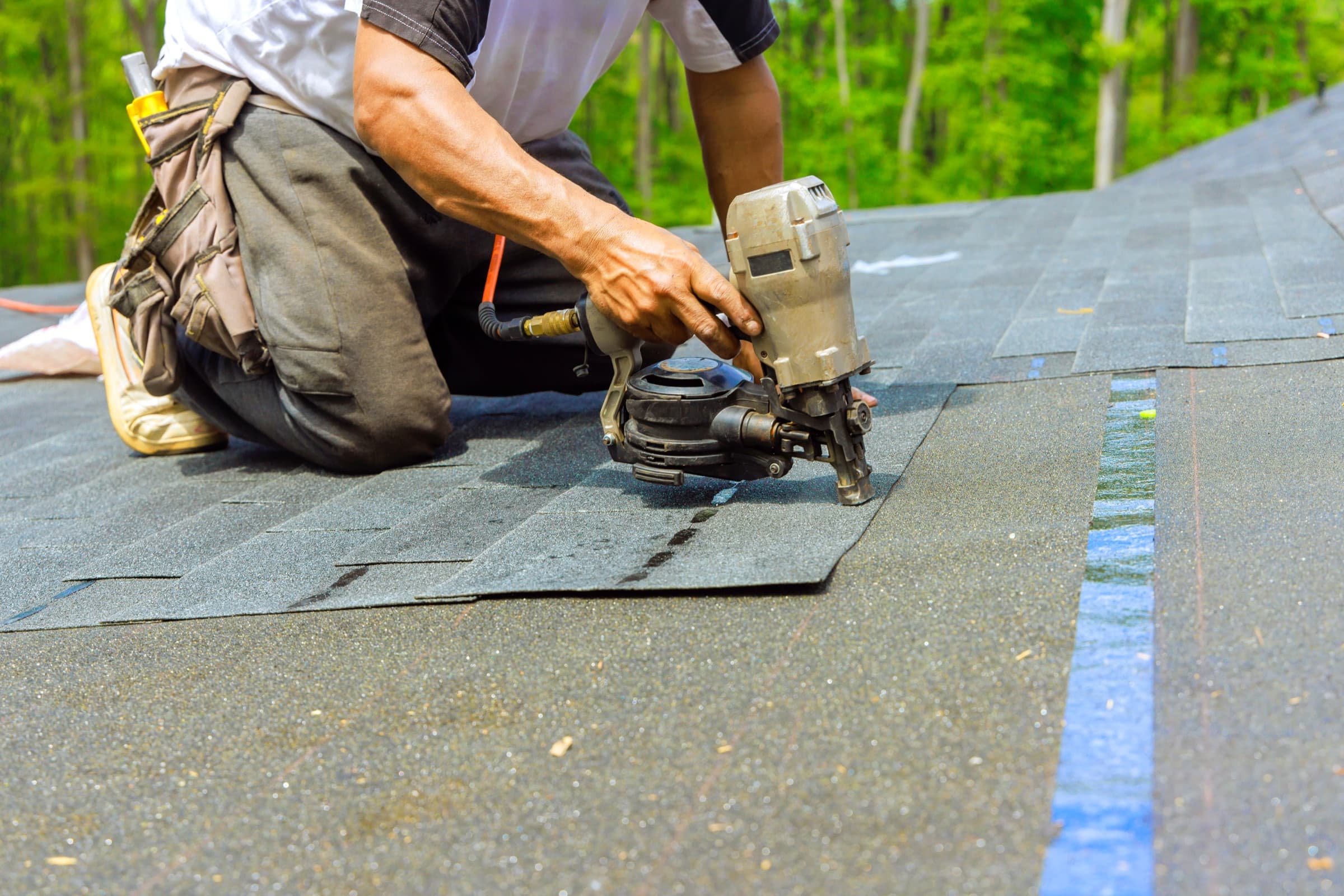 Roofing contractor fastening shingles with a pneumatic nail gun during installation.